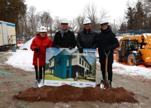 4 individuals posing on a mound of dirt preparing to shovel for groundbreaking ceremony